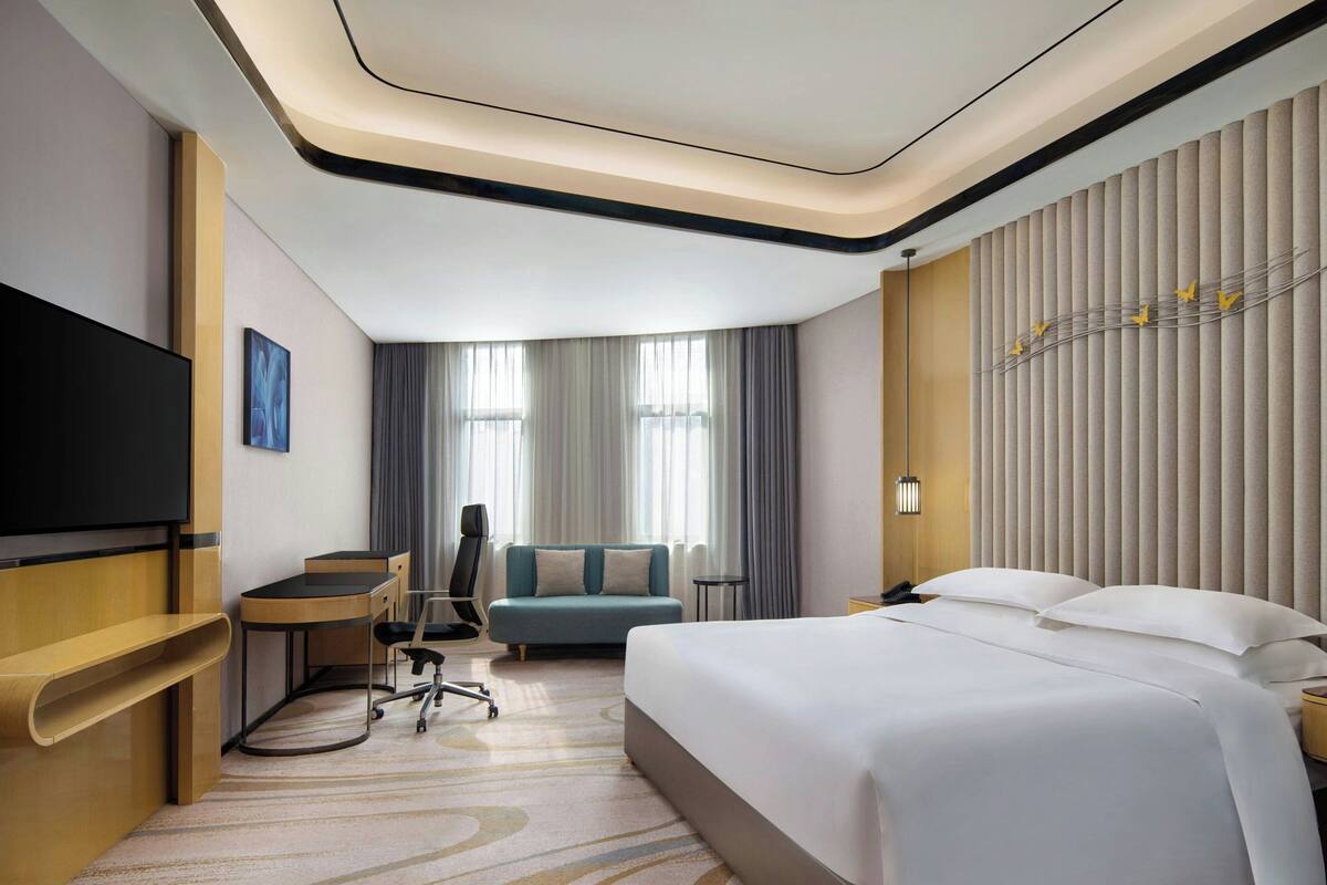 Quarto de hotel com uma cama grande, uma escrivaninha com cadeira, uma televisão de tela plana e um sofá.