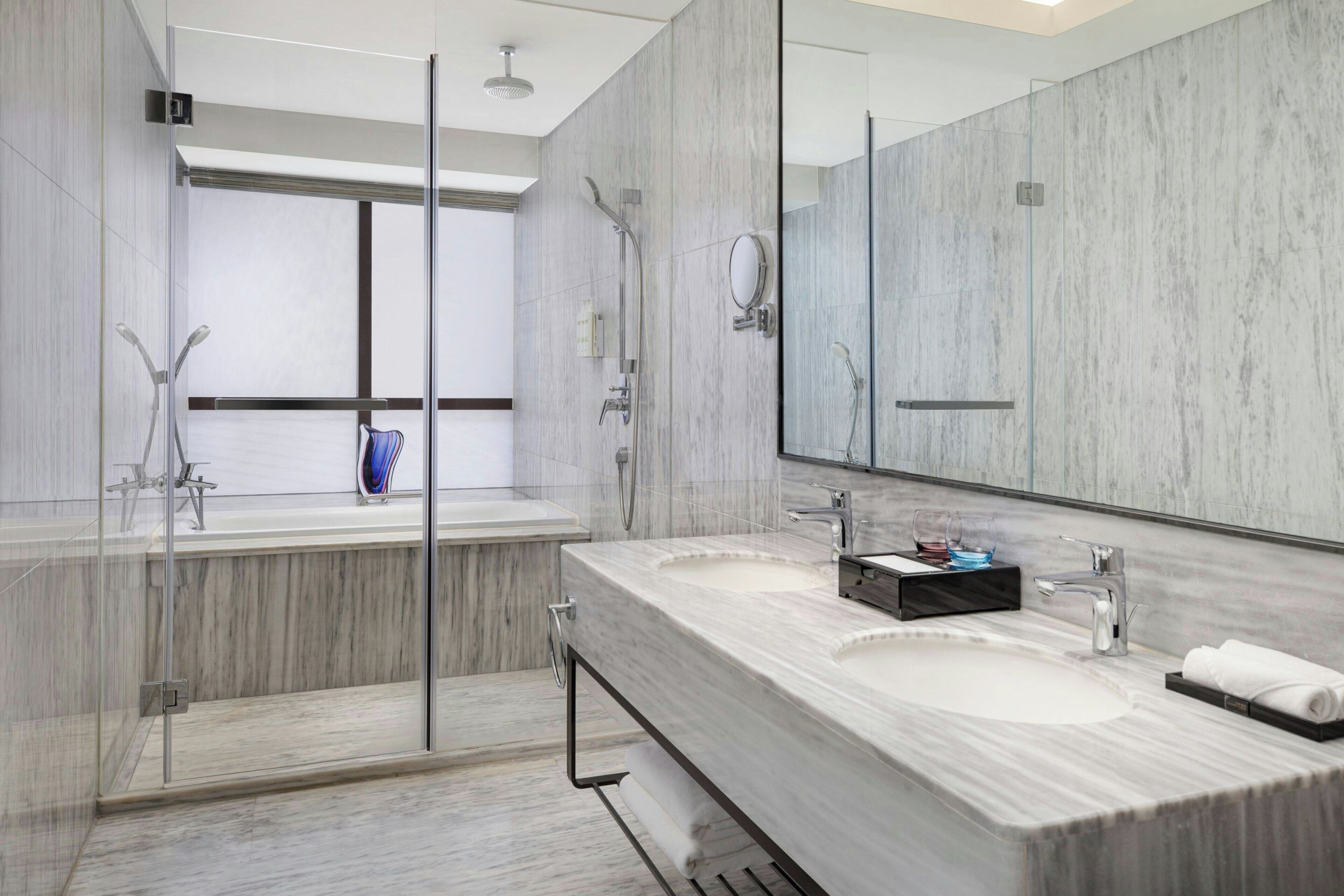 Un baño moderno con dos lavamanos, una cabina de ducha con mampara de vidrio y un espejo grande.