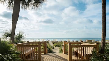 A wooden deck leading to a beach with umbrellas and palm trees.