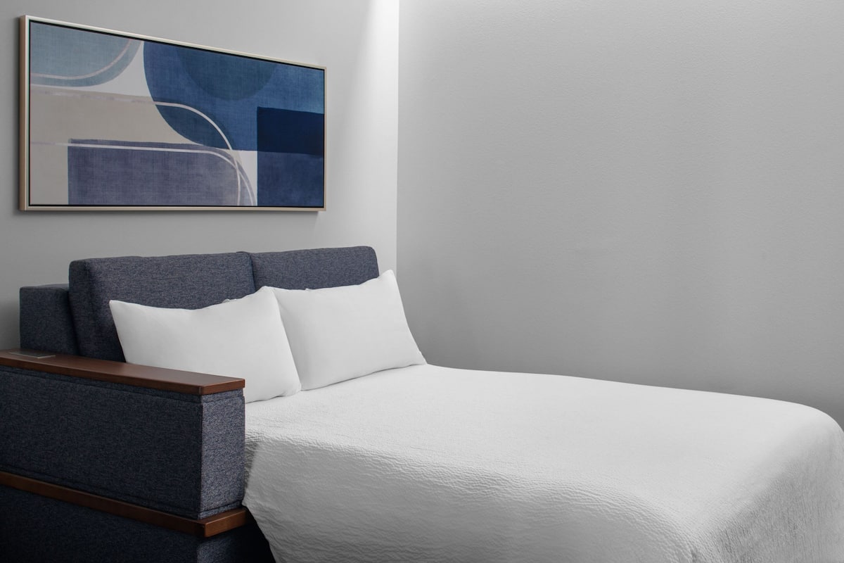 A neatly arranged hotel room with a bed, a nightstand, and a painting on the wall.