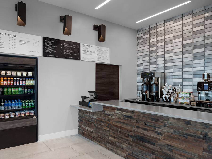 A modern coffee shop interior with a wooden counter, a beverage dispenser, and a menu board.