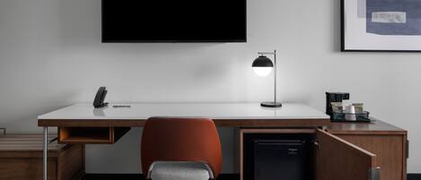 Un bureau moderne équipé d’un téléviseur à écran plat, d’une lampe de bureau, d’une chaise, d’un petit réfrigérateur et d’un classeur.