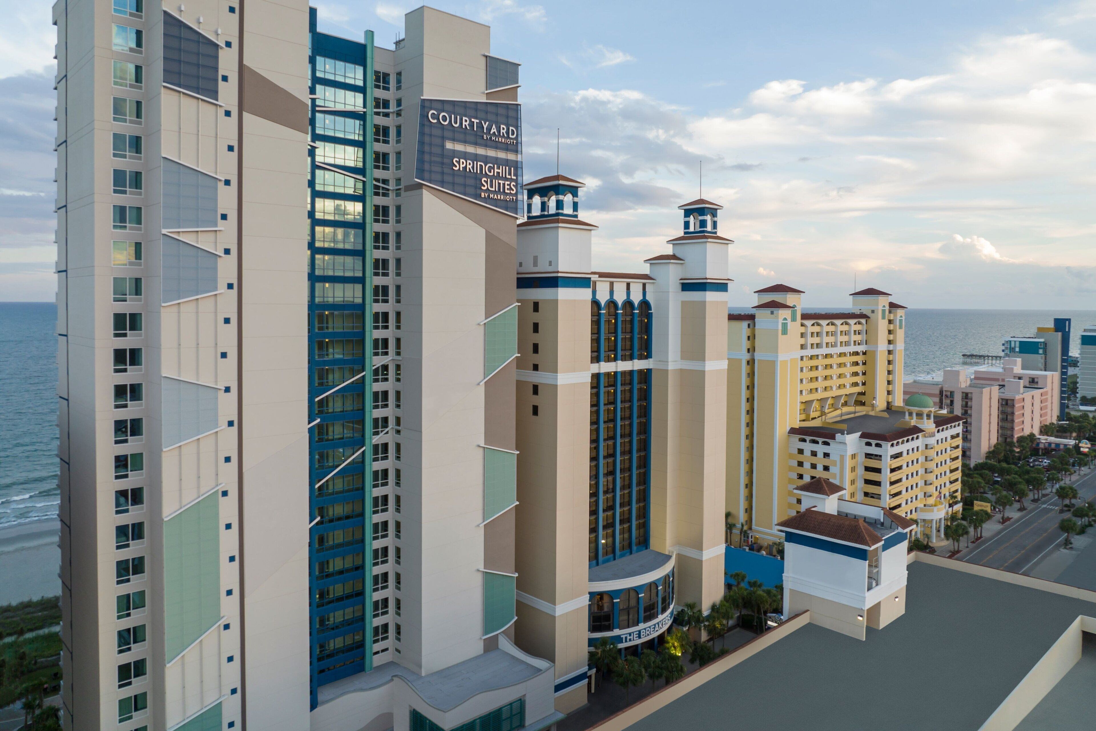 Un hotel con varios edificios altos, un cartel llamativo de 'Courtyard by Marriott Springhill Suites' y vista al océano.
