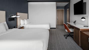 A hotel room with two beds, a desk, a chair, a TV, and a lamp.