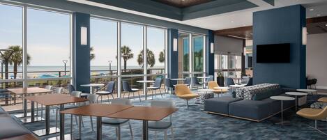 A modern lounge area with large windows, comfortable seating, and a view of the beach.