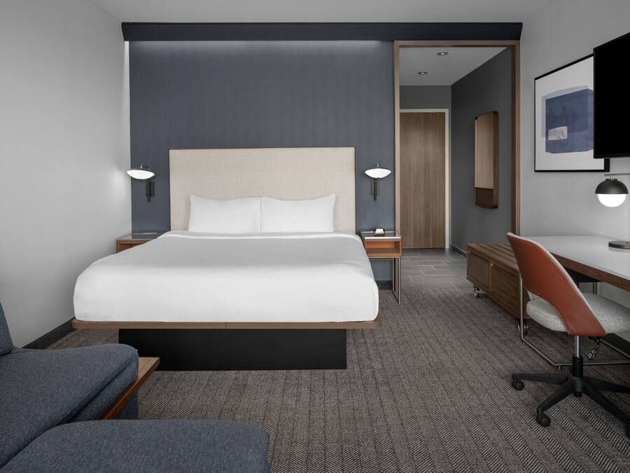 A modern hotel room with a large bed, a desk, a chair, and a television.