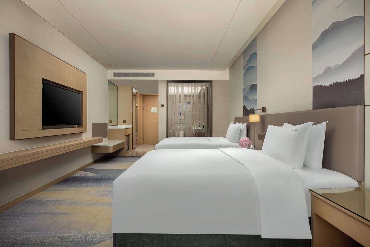 A hotel room with two beds, a flat-screen TV, a desk, and a bathroom.