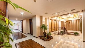 Un vestíbulo de hotel con piso de mármol pulido, un arreglo floral central y una escalera que conduce a un nivel superior.
