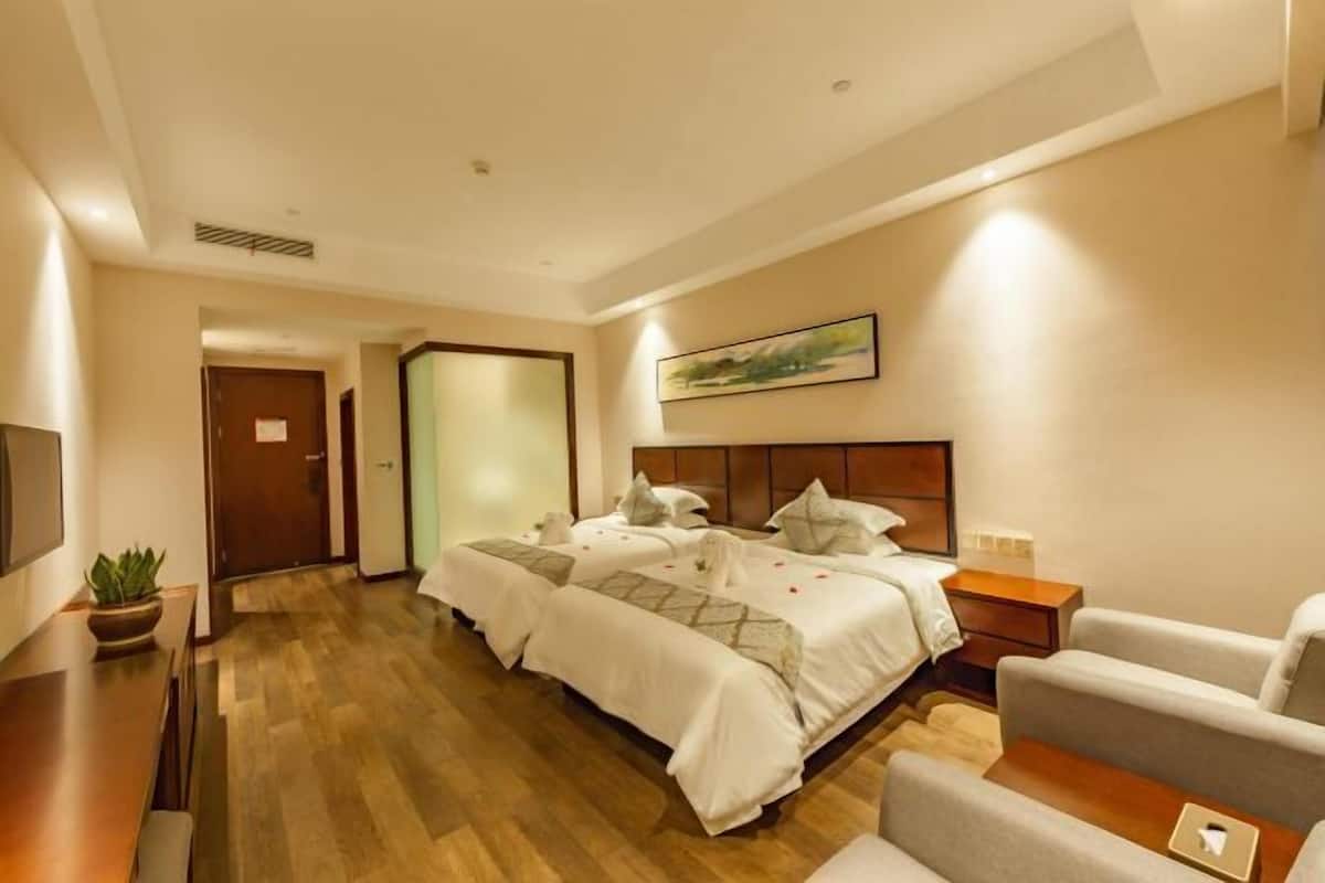 A hotel room with two beds, a desk, a chair, a TV, and a painting on the wall.