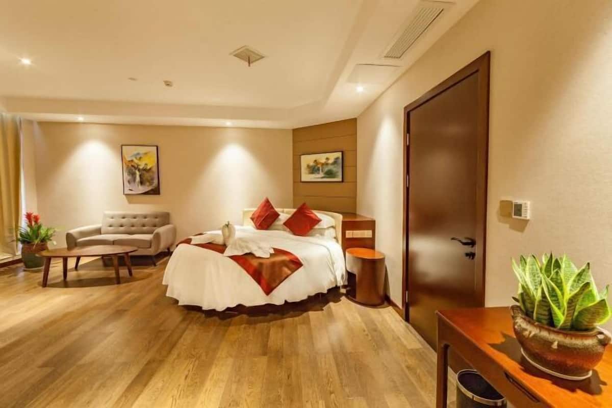 A hotel room with a bed, a sofa, a small table, a potted plant, and a door.