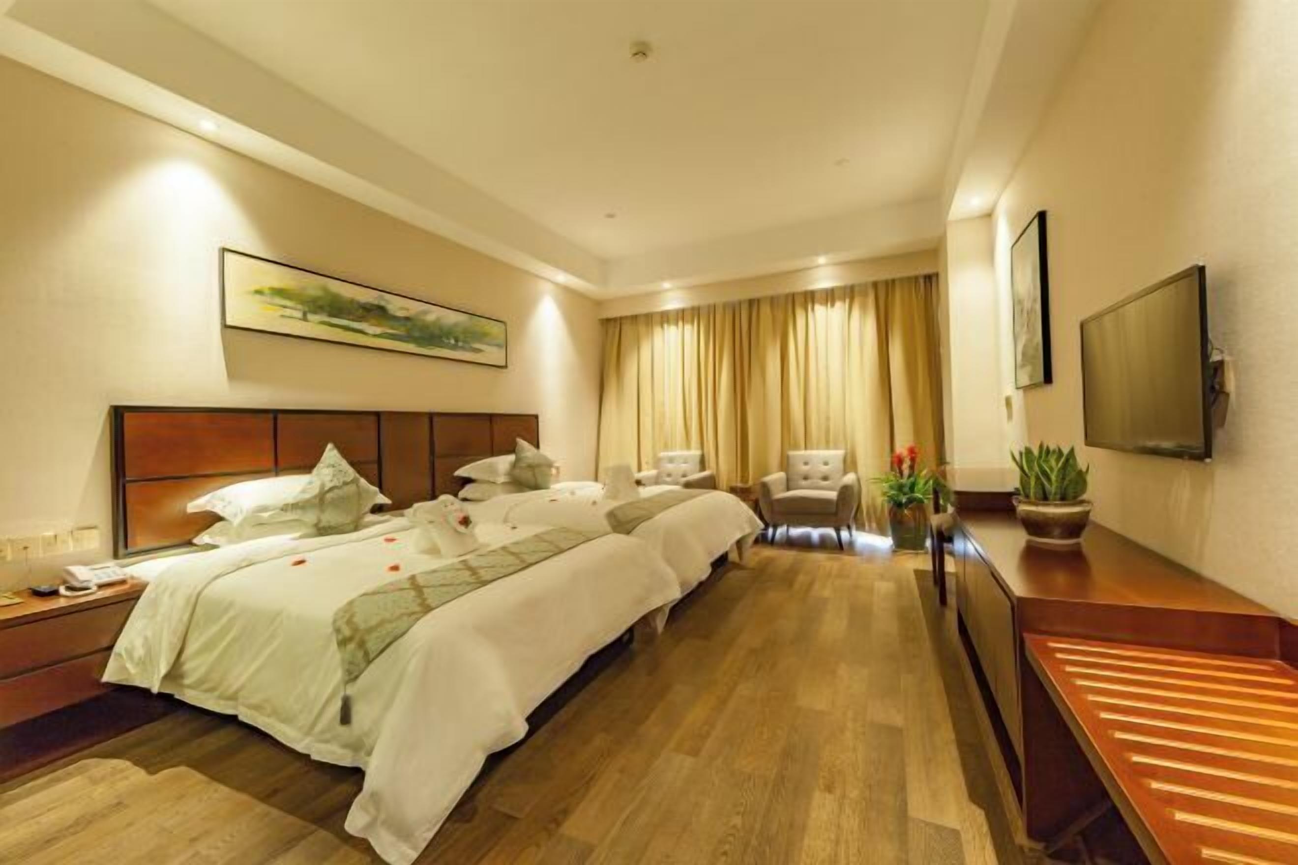 A hotel room with a large bed, a desk, a chair, a TV, and a window with curtains.