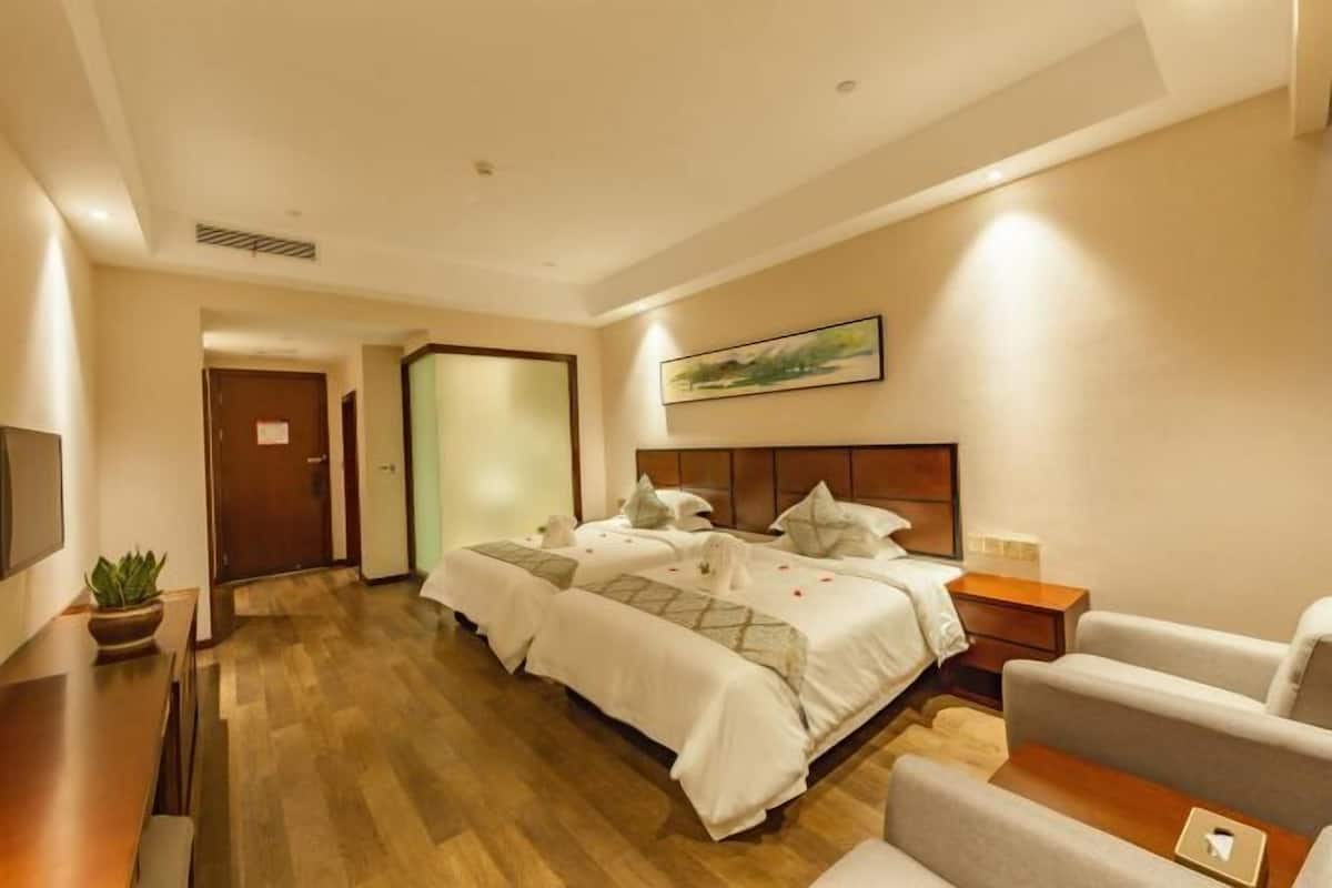 A hotel room with two beds, a desk, a chair, a TV, and a painting on the wall.