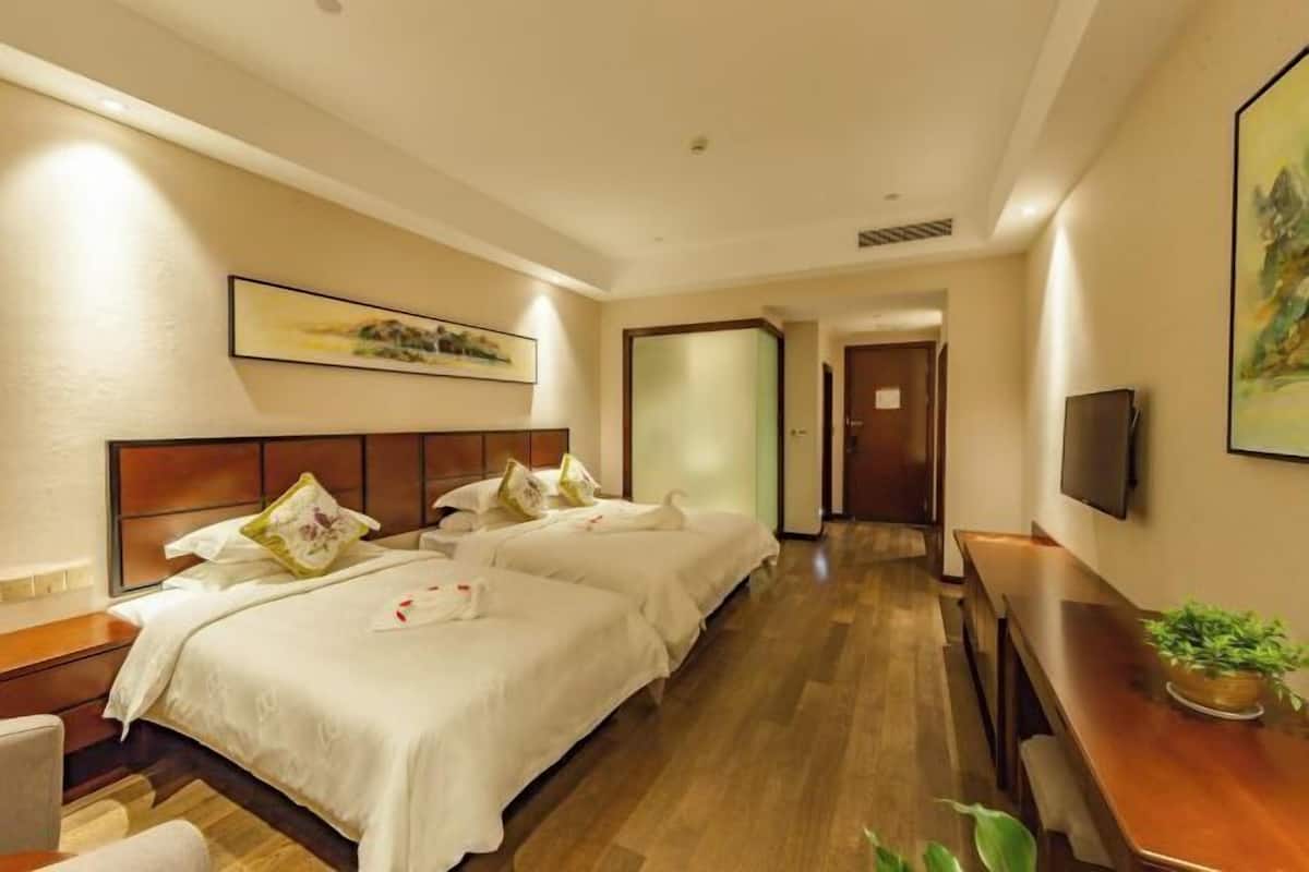 A hotel room with two beds, a wooden desk, a television, and a painting on the wall.