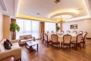 A hotel room with a dining area, a sofa, a coffee table, and a chandelier. - Jing Cheng Hotel (Jiashan)
