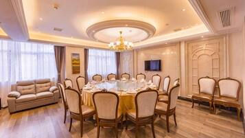 A dining room with a round table, chairs, a sofa, and a television on the wall.