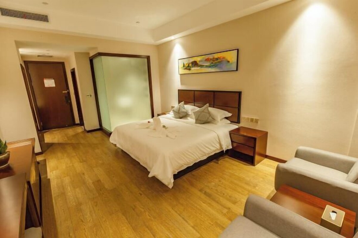 Habitación de hotel con cama, mesita de noche, silla, un cuadro en la pared y una puerta que da a otra habitación.