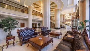 A spacious lobby with a grand staircase, ornate sofas, and a large chandelier.