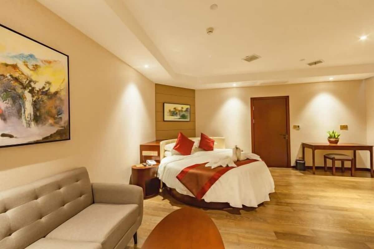 A hotel room with a bed, a sofa, a desk, and a painting on the wall.