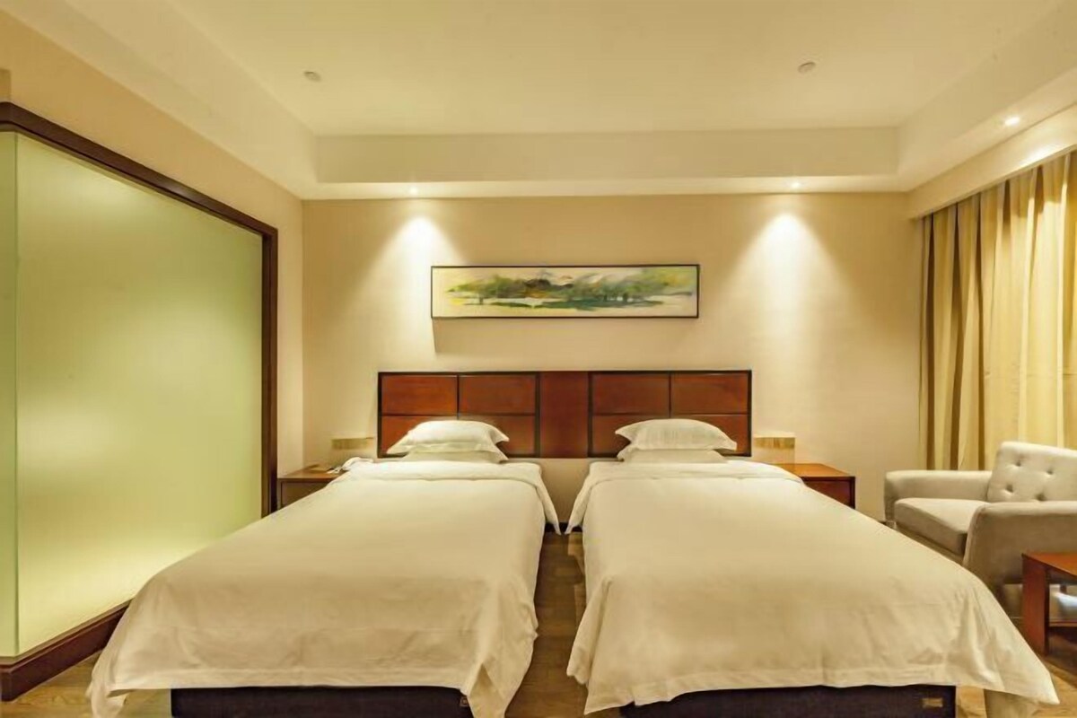 Una habitación de hotel con dos camas, un cabecero, un cuadro, una silla y una mesita de noche.