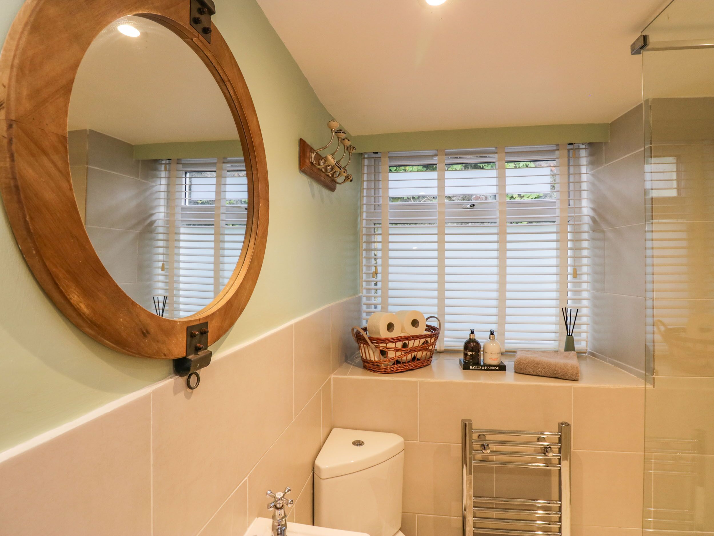 A bathroom with a large mirror, a toilet, a sink, a towel rack, and a window with blinds.