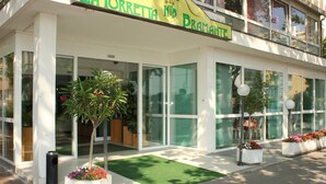 A hotel named "La Torretta Hotel Bramante" with large glass windows, a green entrance mat, and potted plants.