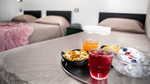 A hotel room with two beds, a table with snacks, a drink, and a fruit container.