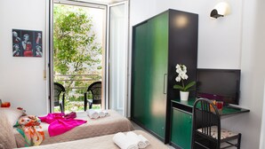 A hotel room with two beds, a desk with a TV, a chair, and a balcony with a chair and potted plant.