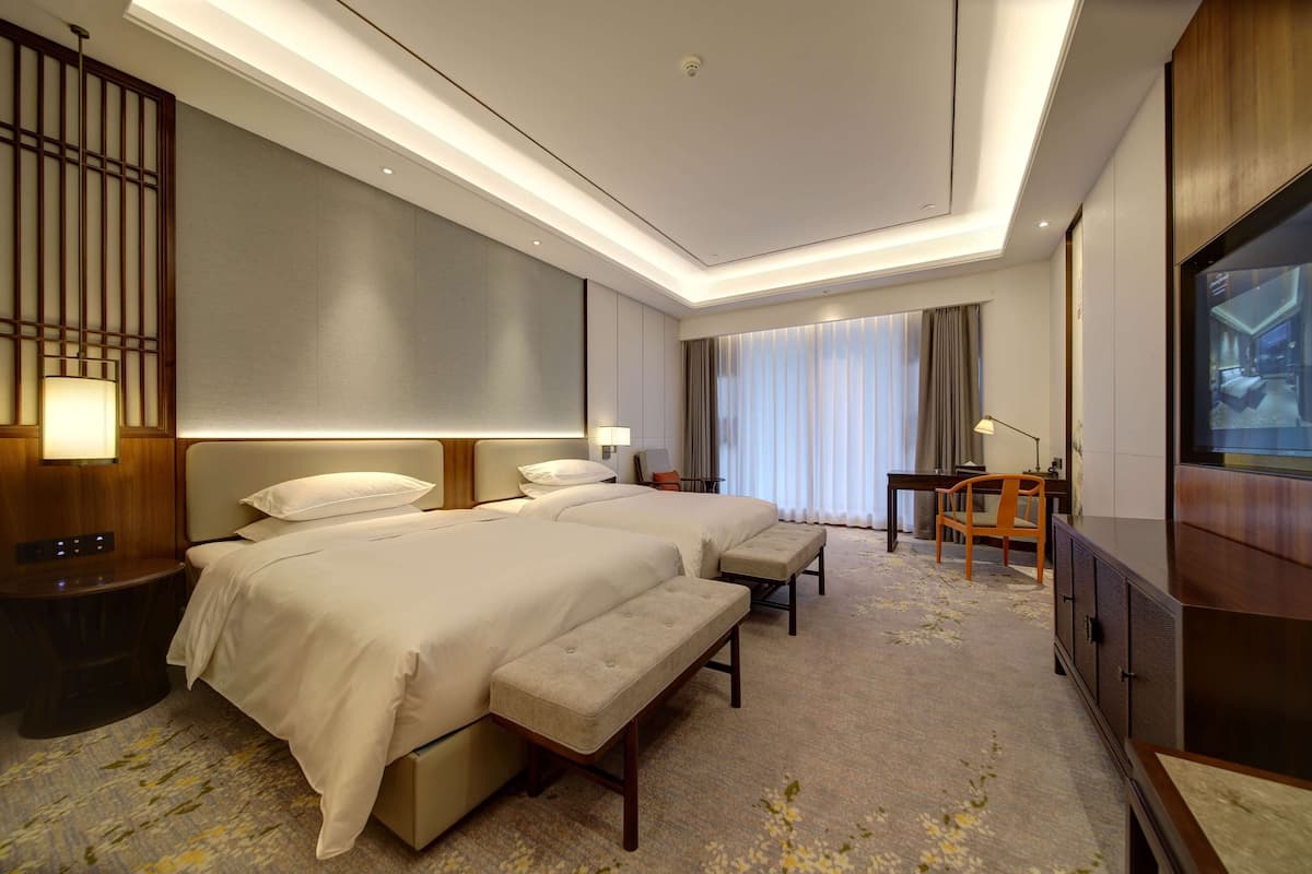 Ein Hotelzimmer mit einem großen Bett, einem Schreibtisch, einem Sessel und einem Fernseher.