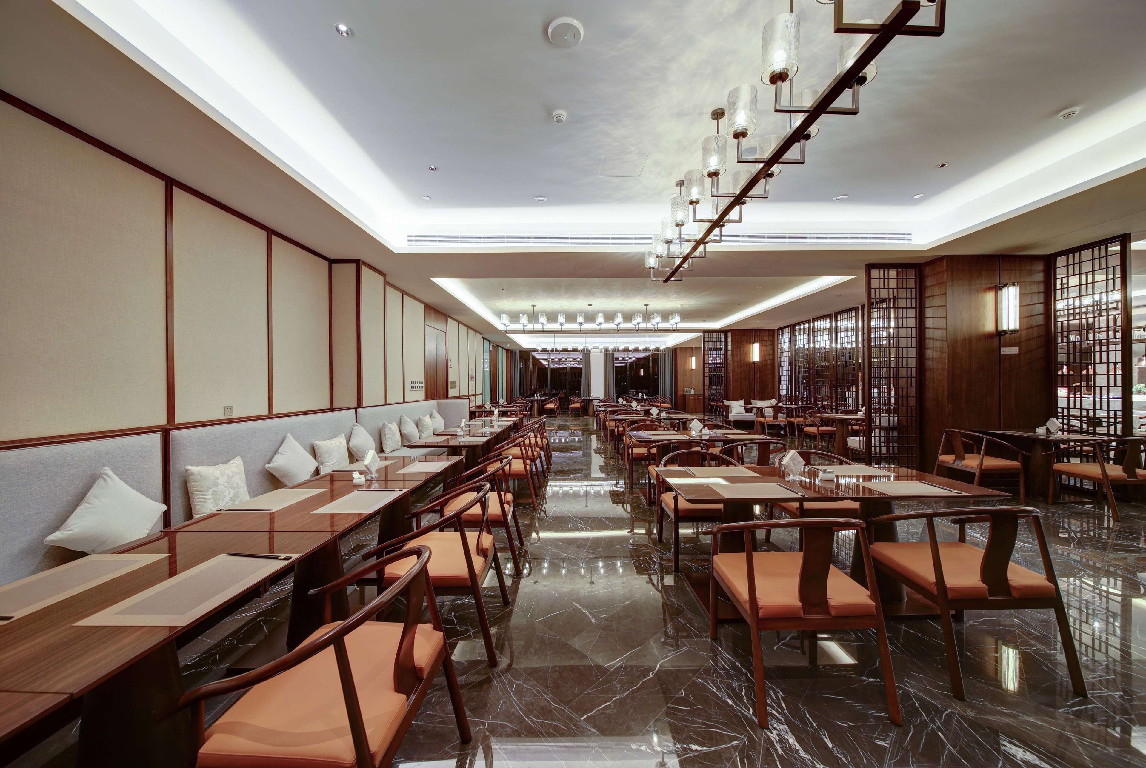 A spacious restaurant with long tables and chairs, a polished marble floor, and a modern chandelier.