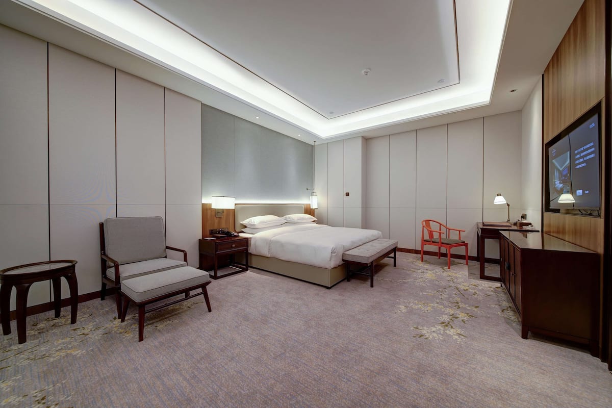 Ein Hotelzimmer mit Bett, Nachttischen, einem Sessel, einem Schreibtisch, einem Fernseher und einem großen Spiegel.
