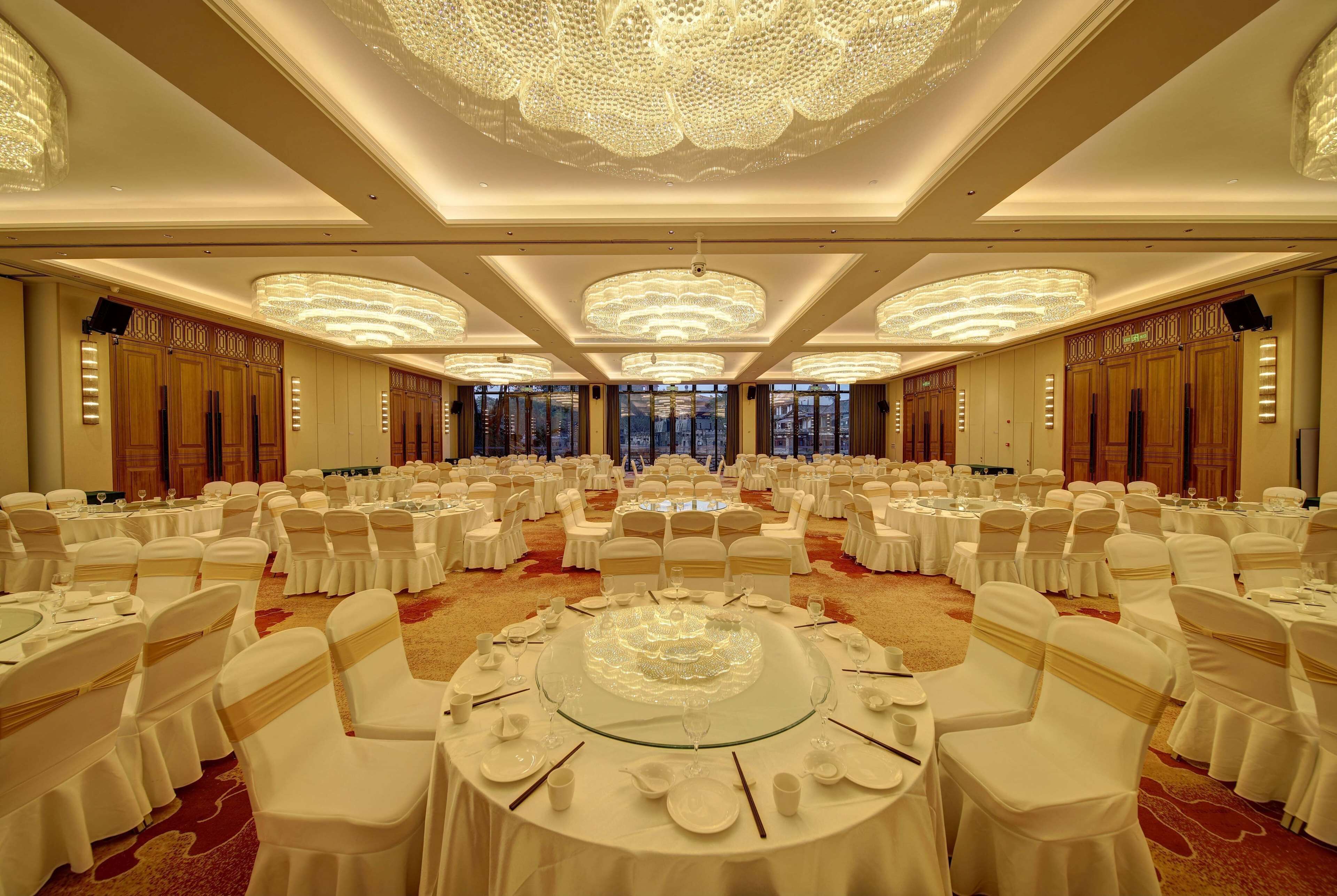 A banquet hall with round tables, white chairs, and chandeliers.