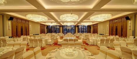 Un salón de banquetes con mesas redondas, sillas blancas y candelabros.