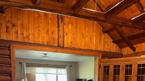 A rustic wooden interior with a dining table and chairs, a kitchen area, and a living space with a sofa and window. - Wrangler Log Cabin Sleep 8 (Condon)