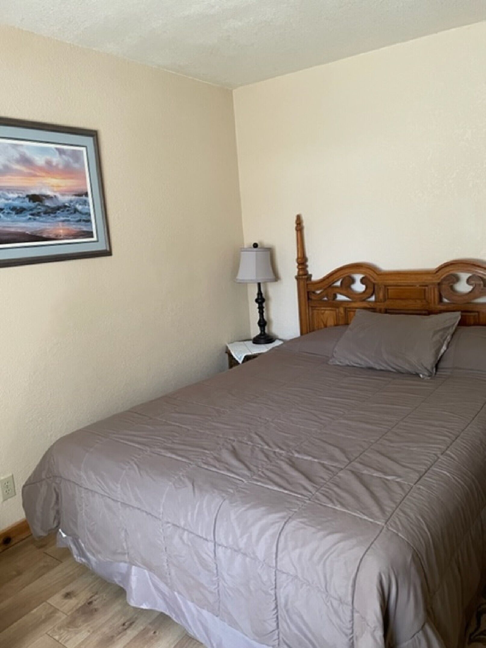 A bedroom with a large bed, a nightstand with a lamp, and a framed picture on the wall.