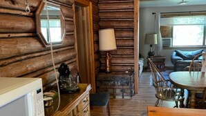 A rustic cabin interior with wooden walls, a dining area with a table and chairs, a kitchen with a microwave, and a window. - Wrangler Log Cabin Sleep 8 (Condon)