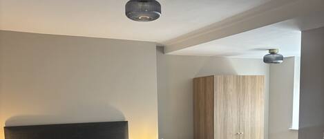 A bedroom with a bed, bedside table, lamp, wardrobe, and a desk with a chair.