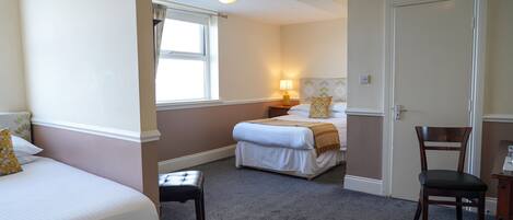 A hotel room with two beds, a chair, a nightstand with a lamp, and a window.