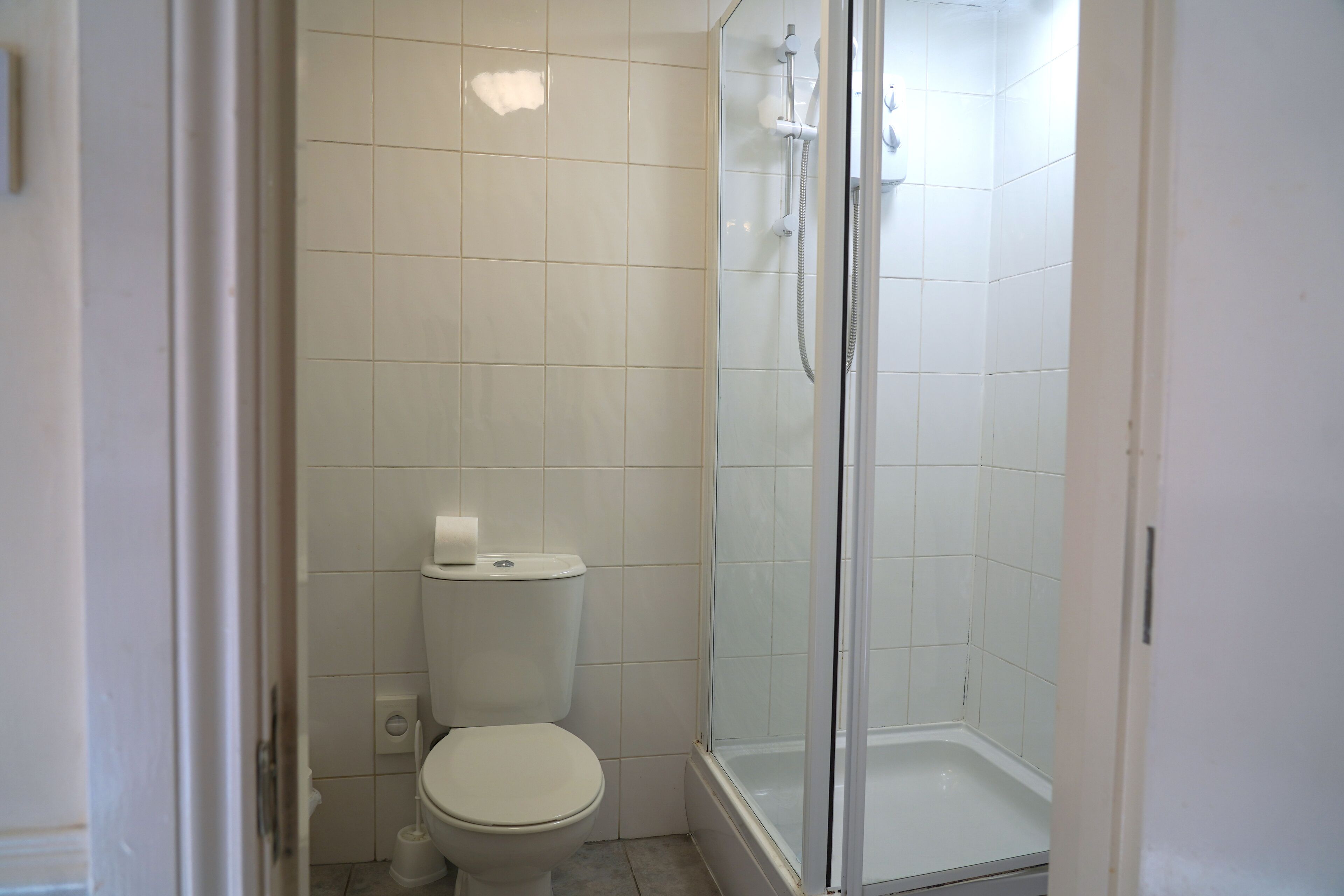 Ein Badezimmer mit Toilette, einer Duschkabine und weiß gefliesten Wänden.