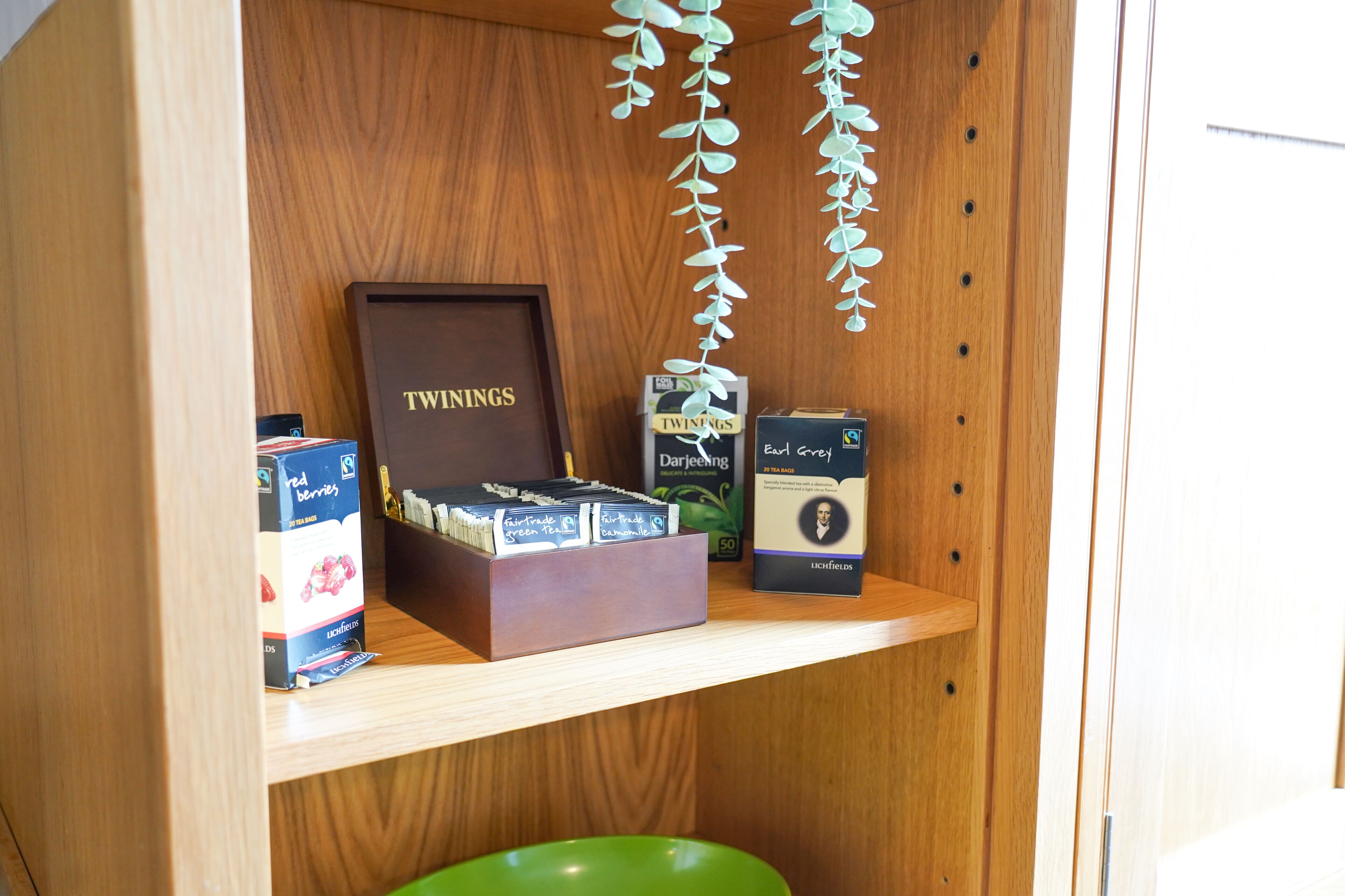 Egy fából készült polc, rajta egy keretezett tárgy, amelyen a „TWINDINGS” felirat látható, egy doboz „Fairtrade Green Tea” (igazságos kereskedelmi zöld tea), és egy „Carl Grey” teásdoboz.