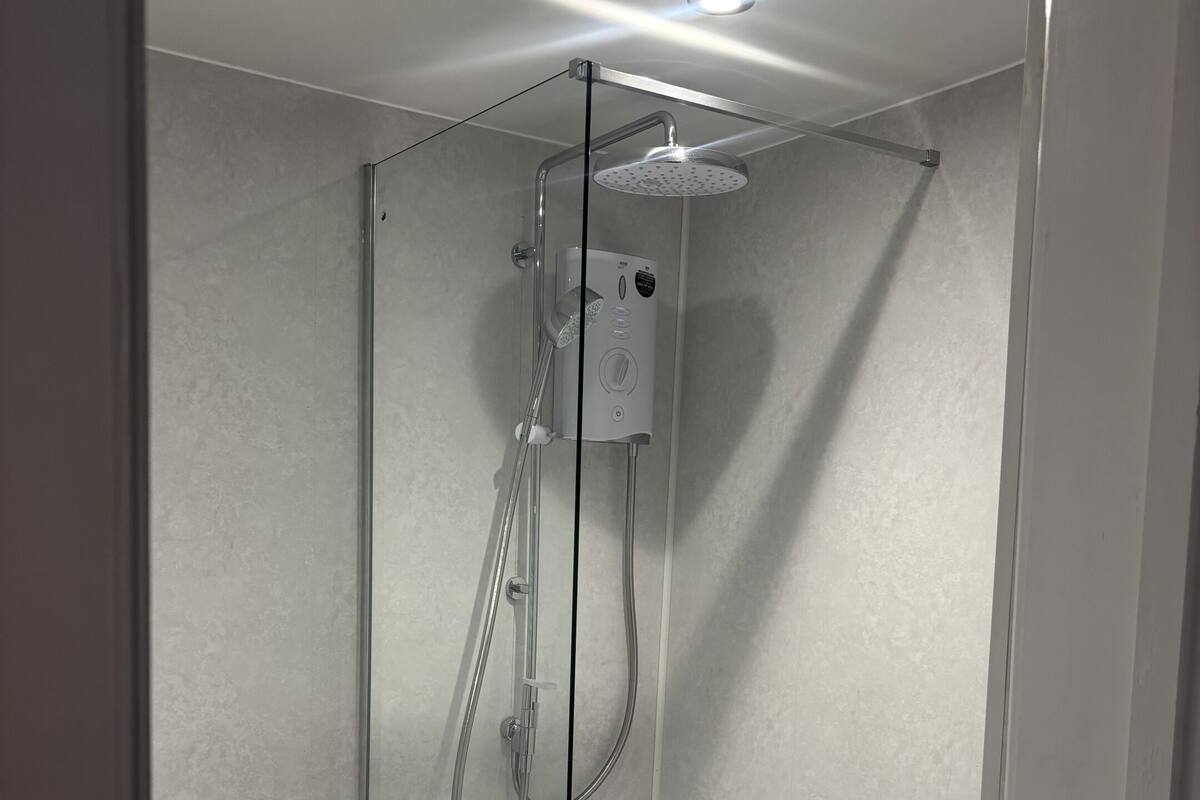 Een moderne badkamer met een douchecabine van glas, een toilet en een klein opbergruimte met toiletartikelen.