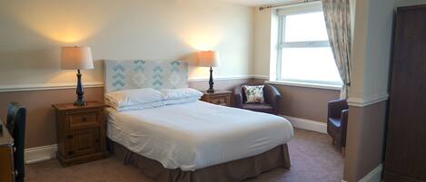 A bedroom with a large bed, two bedside tables with lamps, a window with curtains, and a chair.