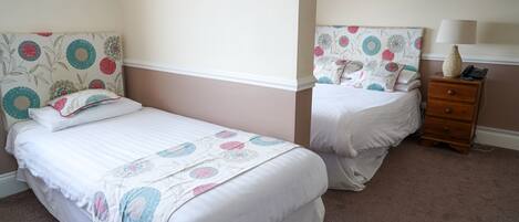 A bedroom with two beds, each with floral headboards and white bedding. There is a wooden nightstand with a lamp and a telephone.