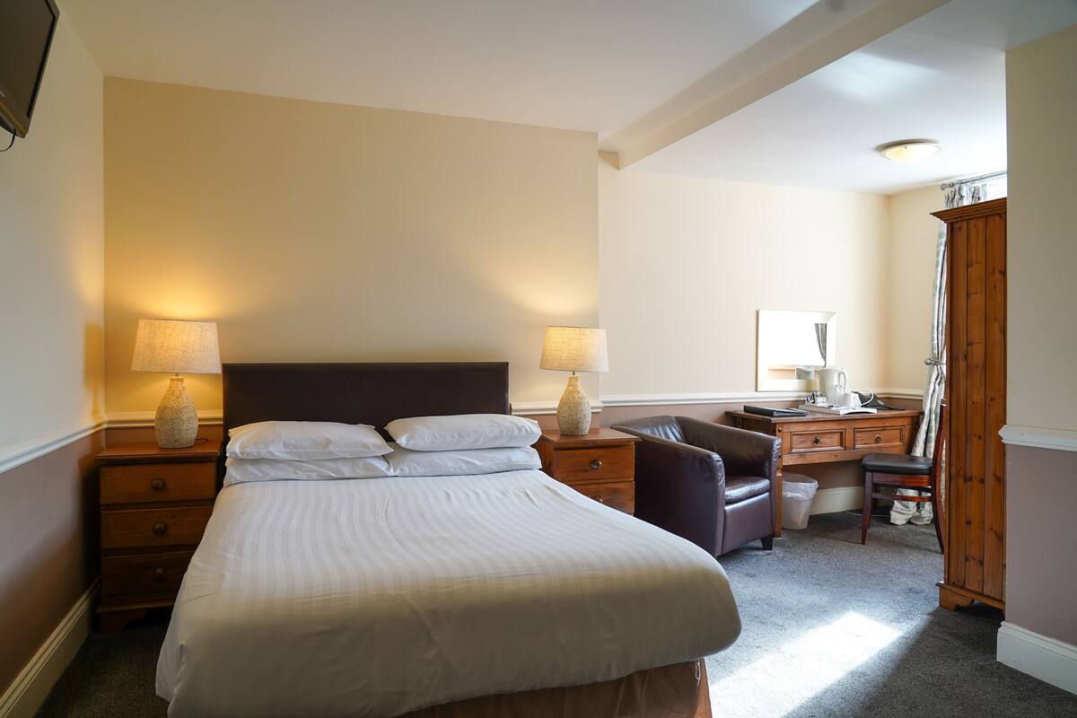 Een hotelkamer met een groot bed, twee nachtkastjes met lampen, een bureau, een stoel en een garderobe.