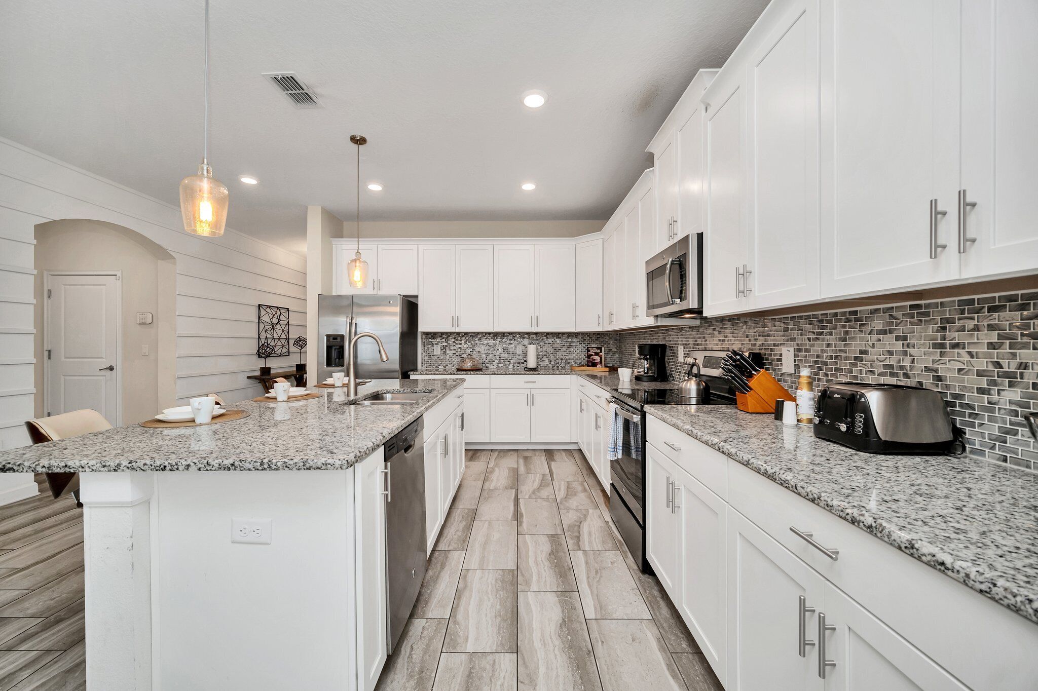 A modern kitchen with white cabinetry, granite countertops, a stainless steel refrigerator, and a tiled backsplash.