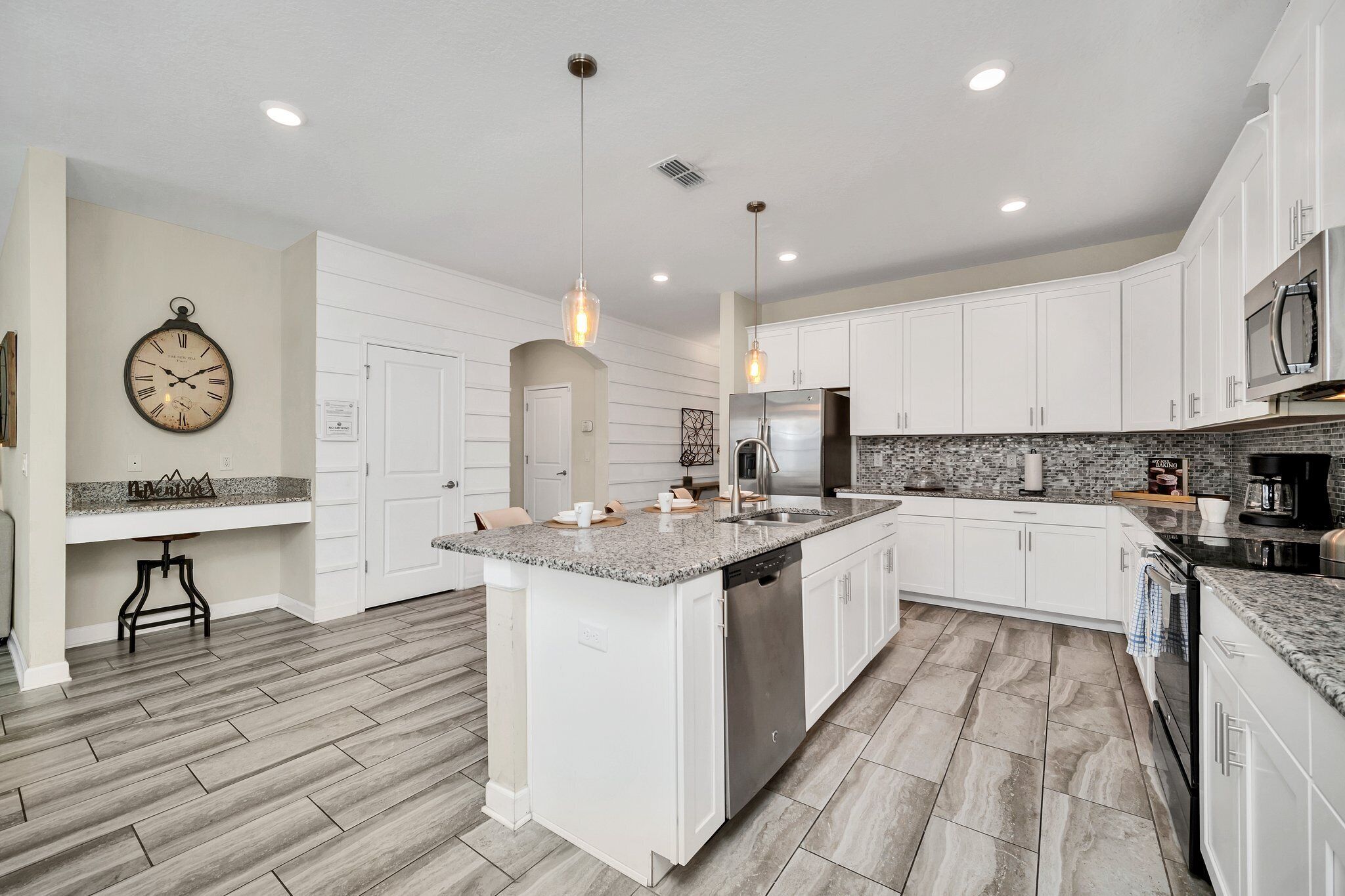 A modern kitchen with white cabinets, a granite countertop, stainless steel appliances, and a central island.