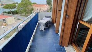 Ein Balkon mit Blick auf das Meer und Gebäude, ein blau gefliestes Podest und eine Holztür.