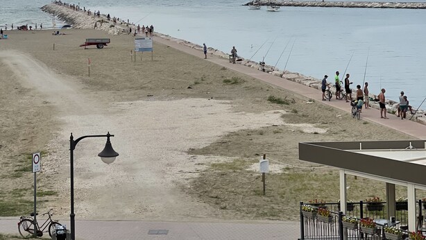 Ein Strandbereich mit einem gepflasterten Weg, einem Fahrrad und einem Gebäude mit Außenbestuhlung.