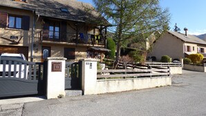 A traditional European-style building with a gated entrance, a balcony, and a mountain backdrop. - T2 on the ground floor of our Villa, (Guillestre)