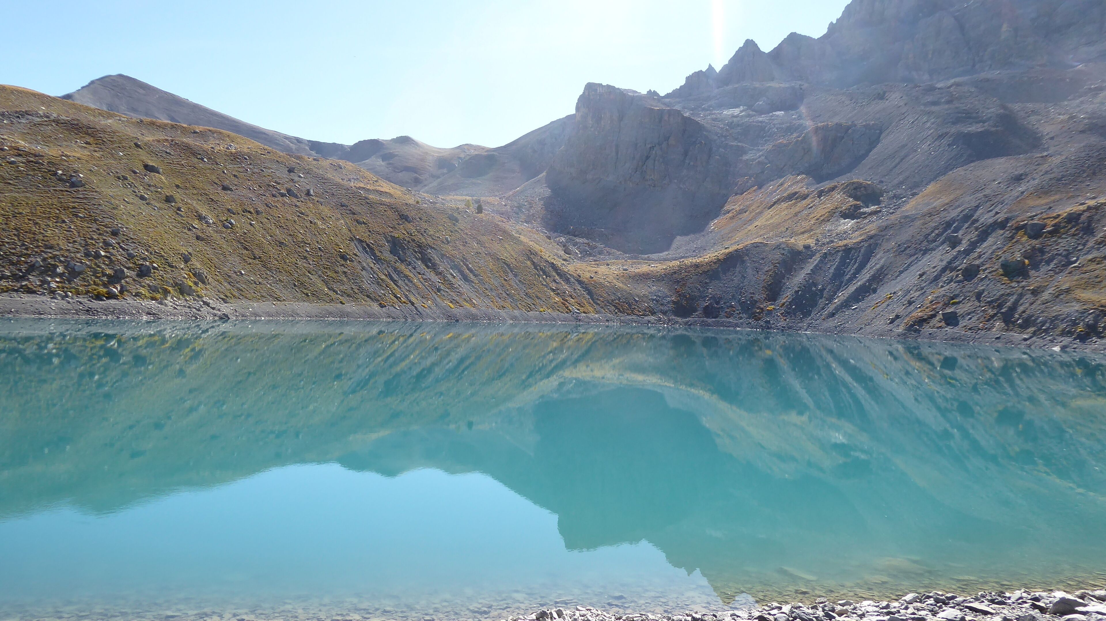 Un llac de muntanya tranquil amb vores rocoses i muntanyes escarpades al fons.