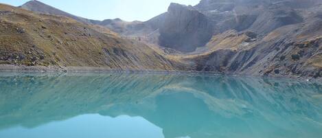 Un llac de muntanya tranquil amb vores rocoses i muntanyes escarpades al fons.